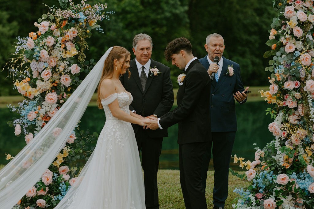 Avery and Timothy exchanging vows in front of a pastel floral arch