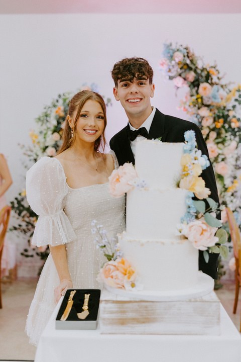 Avery and Timothy with their tiered wedding cake decorated with fresh flowers