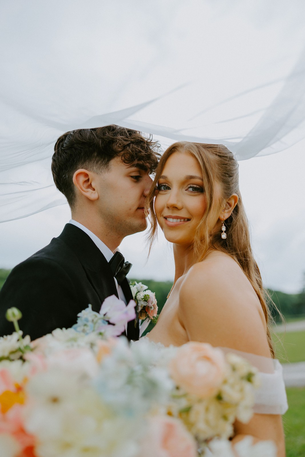 Avery and Timothy close together as her veil blows in the wind